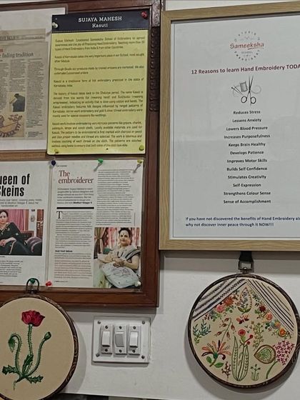 A corner of my studio, featuring press clippings about my work and a framed list of '12 Reasons to Learn Hand Embroidery Today'. Below, two finished hoop art pieces add a touch of handmade beauty.