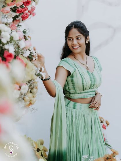 The bride posing by the floral decor at her Haldi ceremony, looking radiant in her green lehenga.