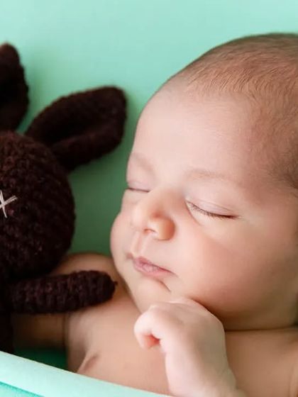A close-up portrait of a sleeping newborn next to a knitted bunny prop, emphasizing their peaceful expression.
