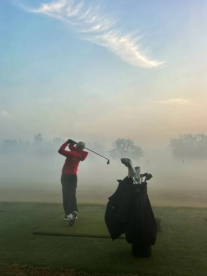 A golfer's swing is captured against the fog and rising sun, creating a truly atmospheric shot.