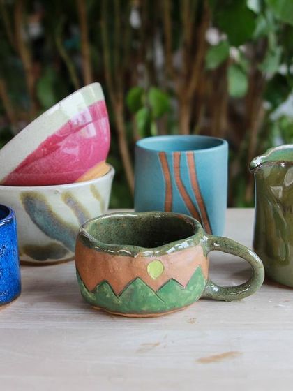 A vibrant assortment of mugs, bowls, and a pitcher, featuring bold colors and playful, hand painted patterns.
