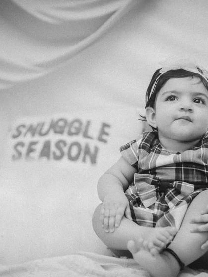 A thoughtful portrait of a baby girl in a "Snuggle Season" setup, rendered in classic black and white for a timeless feel.