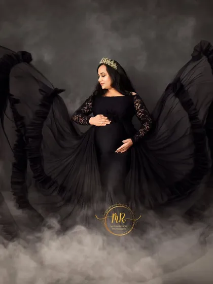 A glamorous solo maternity portrait in a black lace-sleeve gown. The flowing fabric and misty effect at the bottom create a dramatic and enchanting look.