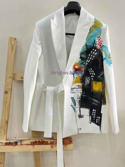 This white belted blazer features a bold, architectural abstract design on one side. The mix of black, yellow, and turquoise creates a modern, edgy look.
