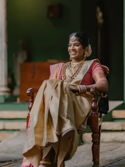 A bride, full of joy, relaxes in an antique chair on the verandah, her golden saree glowing in the soft light.