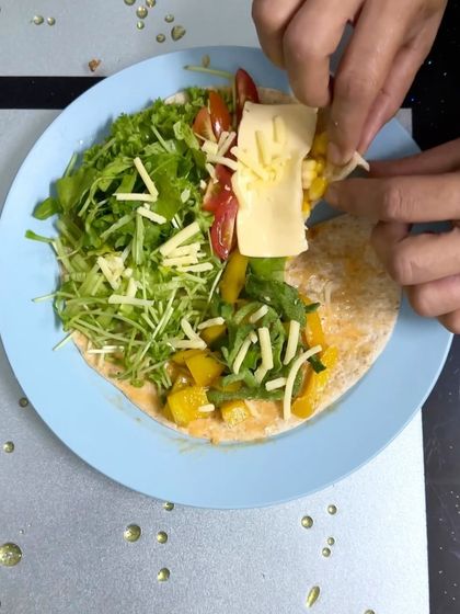 Assembling a vegetarian taco wrap, adding a slice of cheese over a colorful mix of corn, tomatoes, greens, and bell peppers.