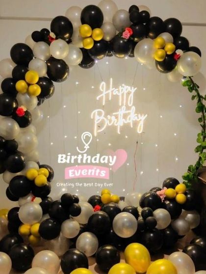 A classic black, white, and yellow balloon ring setup, perfect for any celebration. The addition of green vines adds a touch of nature.