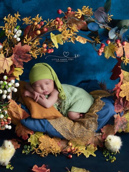 A tiny adventurer in an autumn wonderland. The contrast of the baby's green outfit against the deep blue background and fall leaves is stunning.