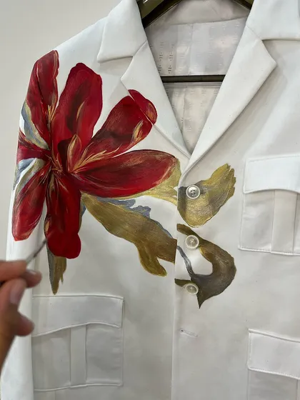 A bold red and gold flower painted on a white multi-pocket blazer. This piece shows how a single, large motif can transform a classic garment into a unique work of art.