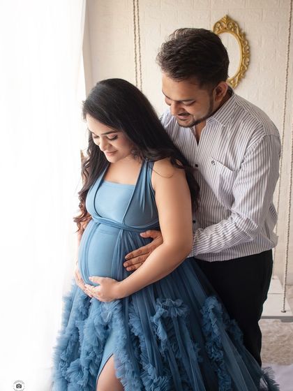 A candid moment between a couple. He looks down at her baby bump with affection as they stand by the studio swing.