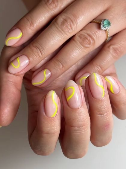 A minimalist abstract design with a single, bright yellow swirl on each nail. This is a great example of how a simple line can make a big impact.