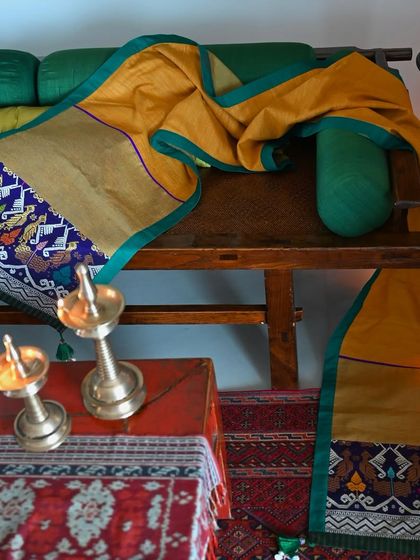 The golden-yellow silk runner styled in a traditional Indian setting with brass lamps. The piece is made from upcycled textiles, giving new life to beautiful old fabrics.