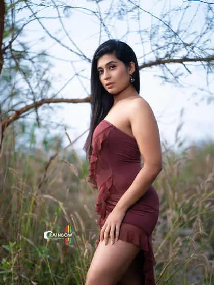 A fashion shoot in a field of tall grass. The earthy tones of the background contrast beautifully with the model's maroon dress, creating a moody and atmospheric portrait.