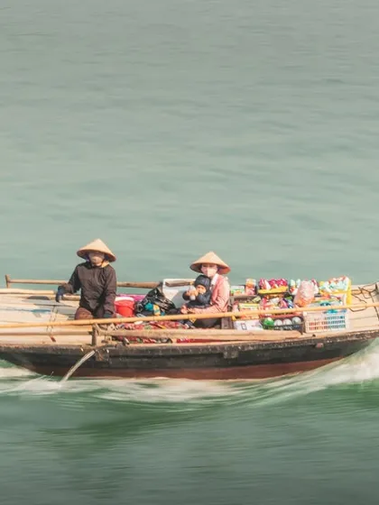 Two vendors in a small boat in Halong Bay, captured with a slow shutter speed to show their movement across the water.