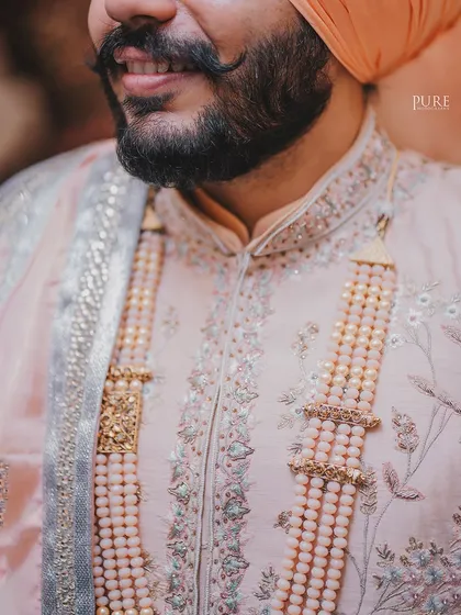 A close-up shot focusing on the intricate details of the groom's wedding attire, from the embroidery on his sherwani to the layers of his mala.