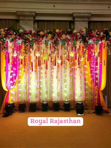 Inspired by "Royal Rajasthan," this Mehendi backdrop uses vibrant pink and yellow drapes with hanging floral strings and traditional lanterns.