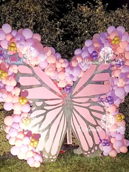 A large, standalone butterfly prop made of wood and decorated with a cascade of pink and purple balloons, creating a stunning photo feature.