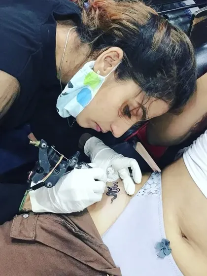 This is what my training is all about: hands-on experience. Here, a student is practicing her line work, tattooing a small snake design on a client under my supervision in a real studio setting.