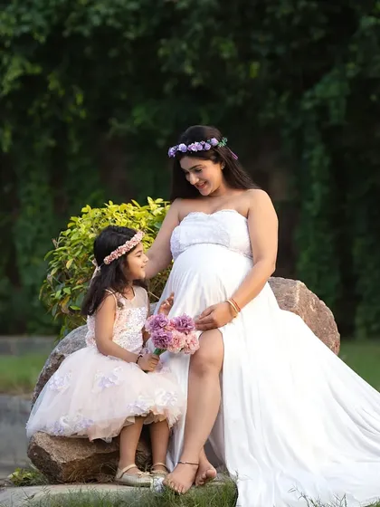 An outdoor maternity portrait with the older daughter, both wearing coordinating floral crowns. Outdoor settings provide a soft, natural light for these special family moments.