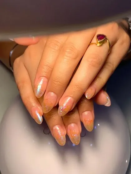 A simple and shimmery set of almond-shaped nails with a sheer base and encapsulated orange glitter.