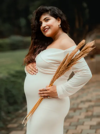 A graceful side-profile portrait of the mother-to-be, holding dried wheat stalks that add a rustic and natural element to the photograph.