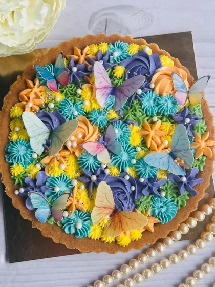 A decadent dark chocolate tart crowned with a silky egg-free meringue buttercream in beautiful pastel shades, edible pearls, and charming edible butterflies.