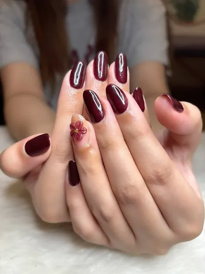 A full view of the elegant maroon manicure with its single floral accent.