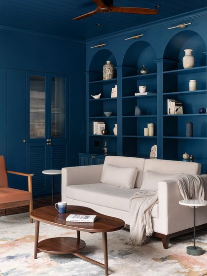 We transformed this room into a library drenched in a deep indigo blue, creating a cozy and dramatic mood. The custom arched bookshelves are filled with curated white pottery, and the space is furnished with a neutral sofa and a leather armchair for comfort.