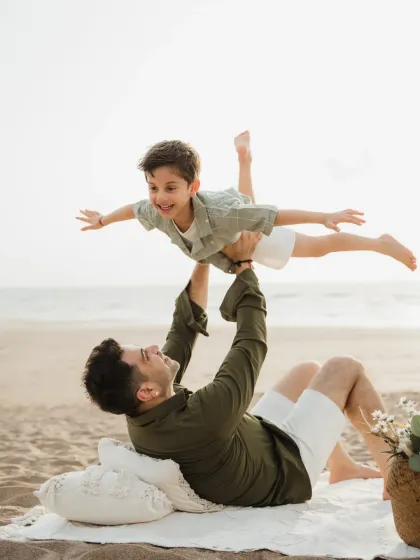 A father playfully lifts his son in the air while lying on the sand. This "airplane" pose is always a hit with kids during beach photoshoots.