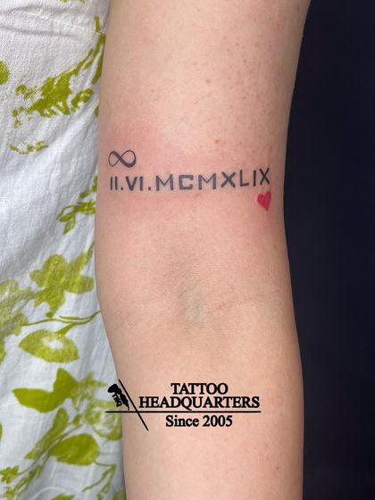 A tattoo of a significant date in Roman numerals, "II.VI.MCMLIX," flanked by an infinity symbol and a heart.