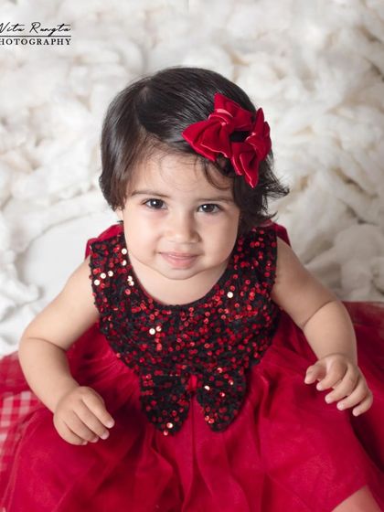 A beautiful close-up portrait of a baby girl, where her expressive eyes and the festive red bow are the stars of the shot.