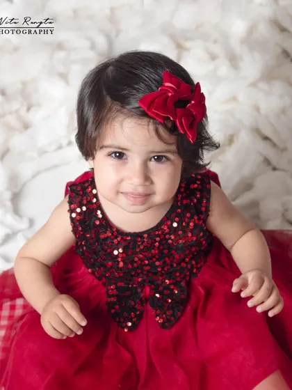 A beautiful close-up portrait of a baby girl, where her expressive eyes and the festive red bow are the stars of the shot.