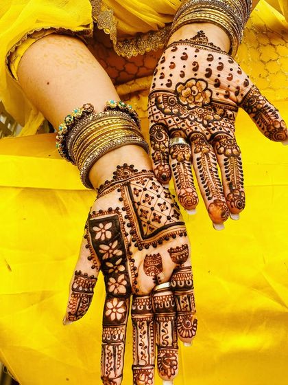 A festive design with intricate patterns on the fingers and a mix of floral and geometric motifs on the palm. The bright yellow background makes the henna pop.