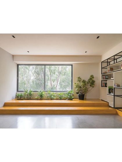 A reading and lounge area in the 'Meraki' clubhouse, with stepped seating by the window that brings in greenery. The built-in shelving provides both storage and display.