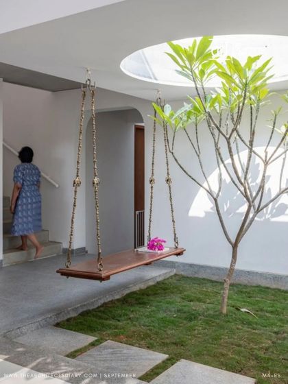 The indoor courtyard with its traditional wooden swing and Frangipani tree, illuminated by a circular skylight. This space is a modern interpretation of a classic Indian architectural element.
