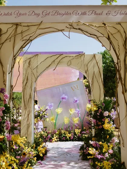 The enchanting entrance to the Haldi ceremony, with a rustic archway and a painted floor, inscribed with "Watch Your Day Get Brighter With Phool & Haldi."