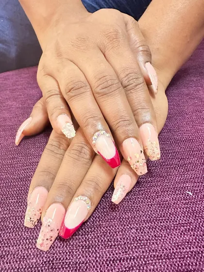 A modern French manicure using a sharp, angled design in hot pink. The look is finished with a line of rhinestones and scattered glitter for extra sparkle.