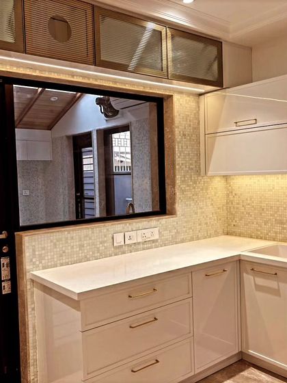 This angle highlights the sink area and the reflection in the window, showing the thoughtful lighting design. The gold-finish handles add a touch of warmth to the white cabinetry.