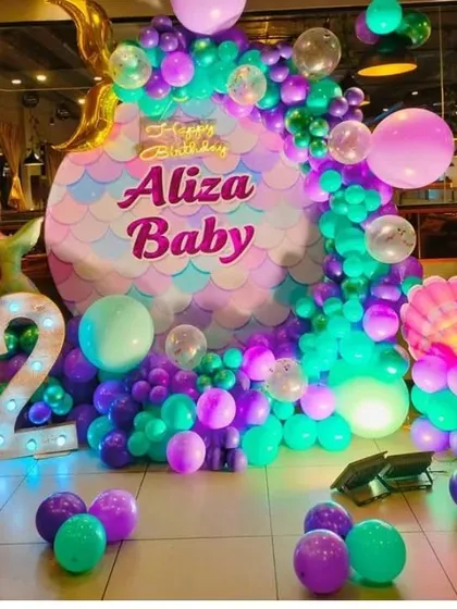 A mermaid-themed second birthday party with a custom-shaped backdrop and a '2' marquee light.