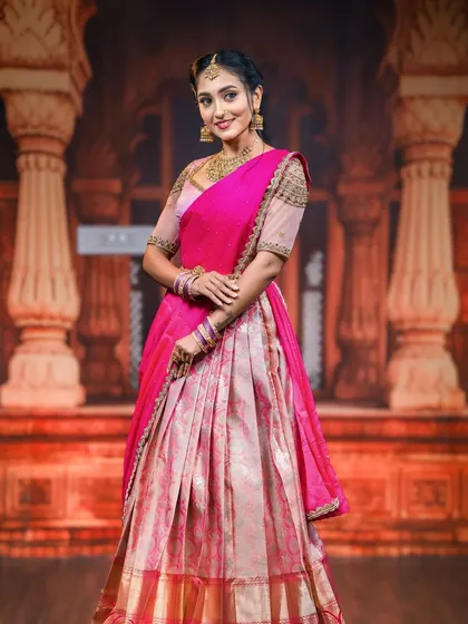 A full-length shot of the model against a traditional backdrop, highlighting the beautiful fall of the half saree and our complementary jewellery.