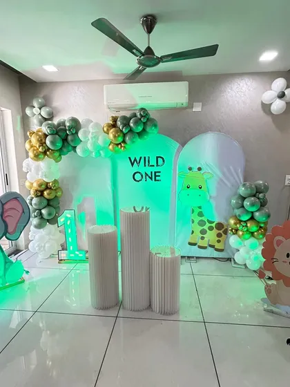A "Wild One" jungle themed decoration for a first birthday at home. This setup features cute elephant and lion cutouts, green and gold balloons, and backdrops with giraffe prints.