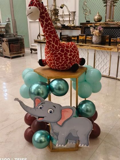 A cute centerpiece for a jungle party, featuring a stuffed giraffe, an elephant cutout, and a balloon arrangement.