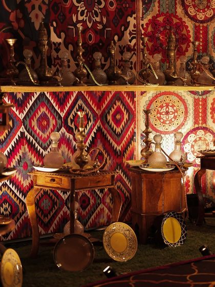 An artifact market setup, featuring brass 'surmadanis' (kohl pots) and glass decanters arranged against a backdrop of vibrant, patterned textiles. This corner was inspired by the treasures found along old trade routes.
