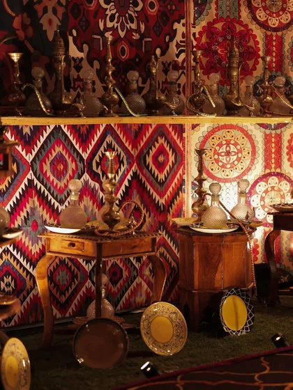 An artifact market setup, featuring brass 'surmadanis' (kohl pots) and glass decanters arranged against a backdrop of vibrant, patterned textiles. This corner was inspired by the treasures found along old trade routes.
