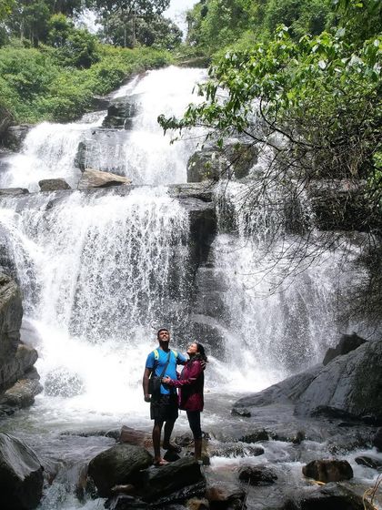 A couple posing for a romantic photo in front of a beautiful waterfall, with the sun kissing them.