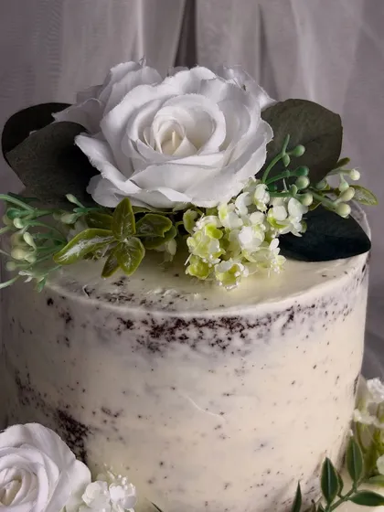 Another angle of the semi-naked cake, focusing on the top tier. The large white silk rose serves as a beautiful focal point, embodying a style that is both rustic and minimalist.