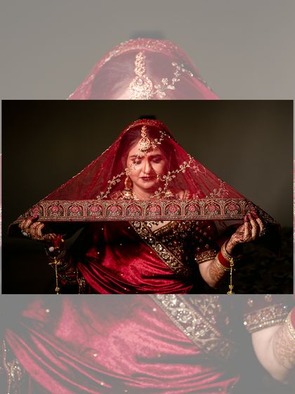 A classic bridal portrait with the bride holding her red veil, creating a frame that draws attention to her expressive eyes and jewelry.