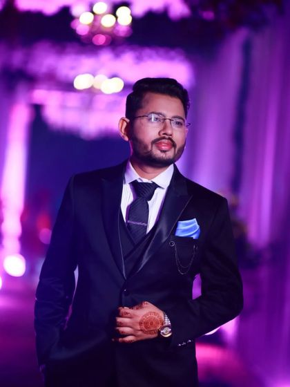 A groom ready for his reception. The purple lighting adds a dramatic effect to his classic black suit and tie.