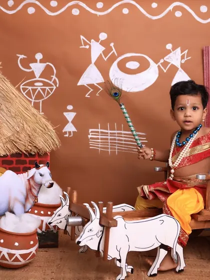 A majestic portrait of a little boy dressed as Krishna. The setup includes a bullock cart, peacock figure, and a vibrant, traditional backdrop, creating a rich and detailed scene.