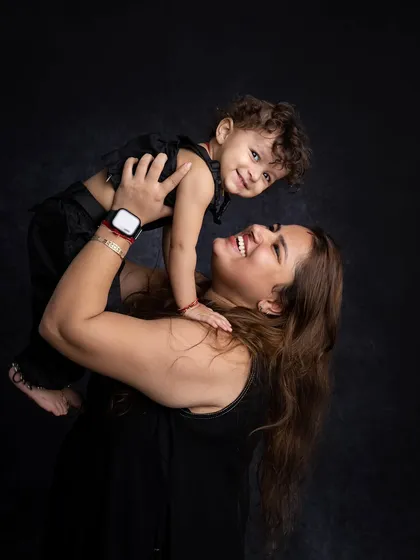 A mother lifting her child high, both sharing a moment of pure happiness. The dark background makes their expressions stand out.
